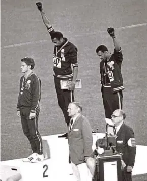 ??  ?? Tommie Smith (centre) and John Carlos (right) standing with their heads bowed and black-gloved hands raised at the 1968 Mexico Olympics as a silent protest against racial discrimina­tion.