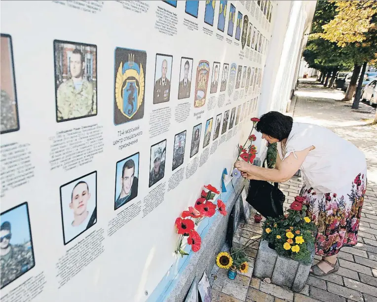  ?? NURPHOTO / GETTY ?? Una mujer deposita flores en el memorial con fotos de soldados fallecidos en Donbass, en el muro externo del monasterio de San Miguel, en una imagen de agosto del 2016