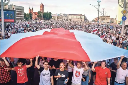  ?? SERGEI GAPON/AFP VIA GETTY IMAGES ?? Protesters hold a giant former white-red-white flag of Belarus used in opposition to the government in central Minsk on Aug. 16.