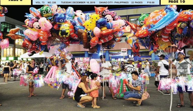  ?? BING GONZALES ?? A FAMILY buys a balloon and toys from one of the vendors who displayed wares at the San Pedro Square. Citizens visit the area every night for the Christmas fairs at the City Hall Grounds.