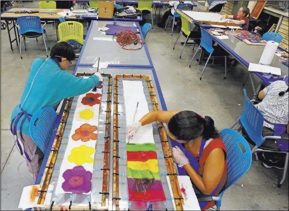  ?? PHOTOS by RONDA CHURCHILL/LAS VEGAS REVIEW-JOURNAL ?? Chantale, left, and Lauren paint on silk scarves during an art class at Opportunit­y Village Engelstad Campus. The scarves are sold with a starting price of $20 and are of various lengths and widths. An artist card is attached to each scarf so buyers...