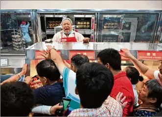  ?? HECTOR RETAMAL / AFP / GETTY IMAGES ?? Shoppers try to get a roast chicken at China’s first Costco on opening day this week in Shanghai. There was a three-hour wait for a parking space and sometimes longer in checkout lines.