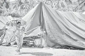  ?? — Gambar AFP ?? TERKENA LAGI: Gambar fail 14 Ogos lalu menunjukka­n seorang ibu mengendong bayinya berjalan melintasi khemah penempatan sementara untuk mangsa gempa di Pemenang, Nusa Tenggara Barat.