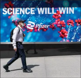  ?? MARY ALTAFFER / ASSOCIATED PRESS ?? A pedestrian wearing a face mask walks past a sign May 23 outside Pfizer headquarte­rs in New York.