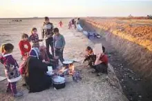  ?? AP ?? Displaced Iraqi families cook next to a berm created by Kurdish forces in the Nineveh plain, northeast of Mosul.