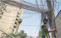  ??  ?? A man checks the wiring on electric cables reaching out to homes in Saadoun Street in the Iraqi capital Baghdad on Sunday. — AFP