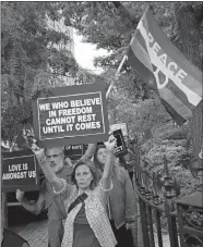  ?? AP PHOTO/MARK LENNIHAN ?? People march around Stonewall National Monument to watch as the Rainbow Flag hangs beneath the American flag on Wednesday in New York. The Rainbow Flag, an internatio­nal symbol of LGBT liberation and pride, was hoisted on a flagpole for the first time...