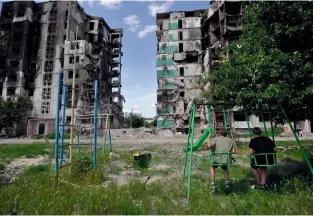  ?? ?? Deux enfants tentent d’oublier le conflit quelques instants sur une balançoire devant leur immeuble détruit à Borodianka, ville située à proximité de la capitale ukrainienn­e, le 7 juin 2022.