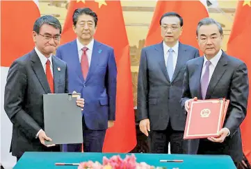  ??  ?? Chinese Premier Li Keqiang, back right, and Japanese Prime Minister Shinzo Abe stand behind Chinese Foreign Minister Wang Yi, right, and Japanese Foreign Minister Taro Kono at a signing ceremony in the Great Hall of the People in Beijing, China.