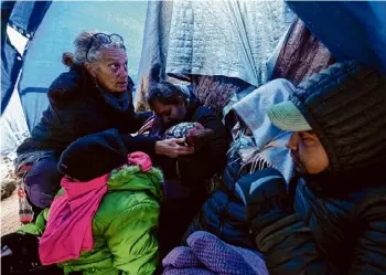  ?? Gregory Bull/associated Press ?? Medical volunteer Karen Parker, left, touches a 2-year-old child with a fever as she talks to a family of asylum-seeking migrants as they wait to be processed in a makeshift, mountainou­s campsite after crossing the border with Mexicoon Feb. 2, near Jacumba Hot Springs, Calif. A federal judge on Friday sharply questioned the Biden administra­tion's position that it bears no responsibi­lity for housing and feeding migrant children while they wait in makeshift camps along the U.s-mexico border.