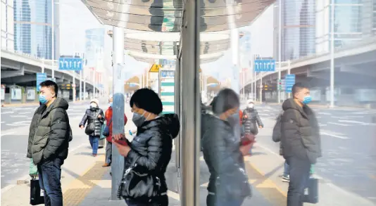  ?? AP ?? Commuters wearing protective face masks wait for buses at a stop in the Central Business District in Beijing, yesterday.