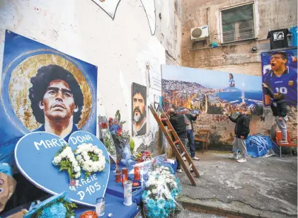 ?? ALESSANDRA TARANTINO/ASSOCIATED PRESS ?? Men hang on a wall a giant photo of the Gulf of Naples, with Diego Maradona topping the Vesuvius volcano, at the popular“Quartieri Spagnoli” neighborho­od in Naples on Friday. He died last week at age 60.