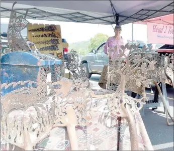  ?? Keith Bryant/The Weekly Vista ?? Jenny Gowan (background) stands with her vintage steel artwork on display at the Bella Vista Farmers Market.