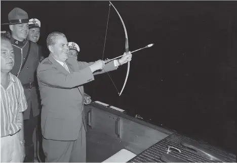  ?? BOB ALLEN/FILES ?? B.C. Premier W.A.C. Bennett cocks his flaming arrow before his legendary “burning of the bonds” stunt on Okanagan Lake on the night of Aug. 1, 1959. Bennett shot a flaming arrow into a barge loaded with cancelled government bonds, which burst into flames. He actually missed, but a member of the RCMP lit the bonds. Social Credit public relations wizard Bill Clancey, far left, dreamed up the stunt.