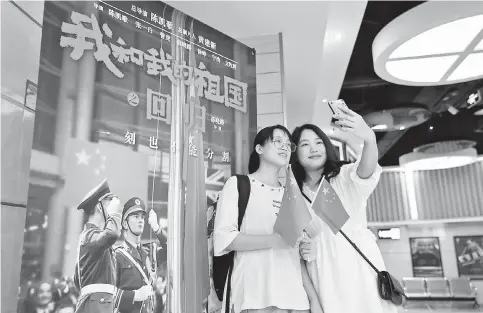  ??  ?? Two moviegoers take selfies with the poster of the movie “My People, My Country” at Shapingba Cinema in Chongqing, Sichuan Province. — IC