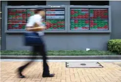  ??  ?? TOKYO: A man walks by an electronic stock board of a securities firm. — AP