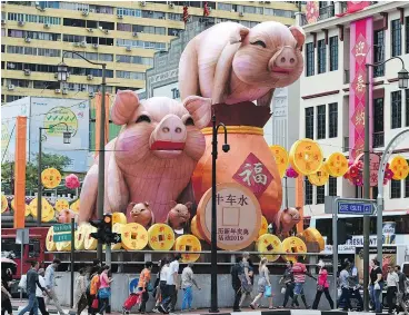  ?? — PHOTO BY ROSLAN RAHMAN / AFP ?? People walk past figurines of the pig for the upcoming Lunar New Year along the roadside of the Chinatown in Singapore earlier this month.