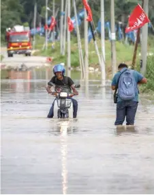  ?? ?? A motorcycli­st attempts to traverse a flooded road resulting from the overflow at Sungai Langat in Kampung Sri Tanjung. — Bernama photo