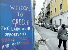  ?? THANASSIS STAVRAKIS/THE ASSOCIATED PRESS ?? A woman and her dog pass graffiti on a wall in Athens, Greece. Greece’s statistics agency says the country has posted a primary budget surplus in 2016, at 3.9 percent of gross domestic product.