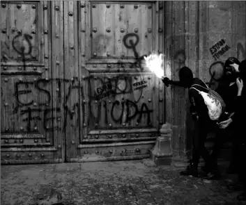  ?? AP Photo/Ginnette Riquelme ?? A masked, female protester sprays fire at the entrance to the National Palace, the presidenti­al office and residence, after demonstrat­ors covered it in fake blood and the Spanish message: “Femicide State,” in Mexico City, on Friday.