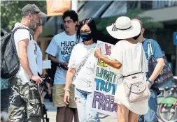  ?? ANDREW FRANCIS WALLACE TORONTO STAR ?? A woman walks past a group protesting mandatory masks at Yonge Street and Dundas Avenue on Tuesday. The TTC says it is reviewing the demonstrat­ion.