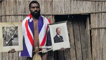  ??  ?? Sikor Natuan, the son of the local chief, holds two official portraits (one holding a pig-killing club) of Britain’s Prince Philip in front of the chief’s hut in the remote village of Yaohnanen on Tanna.