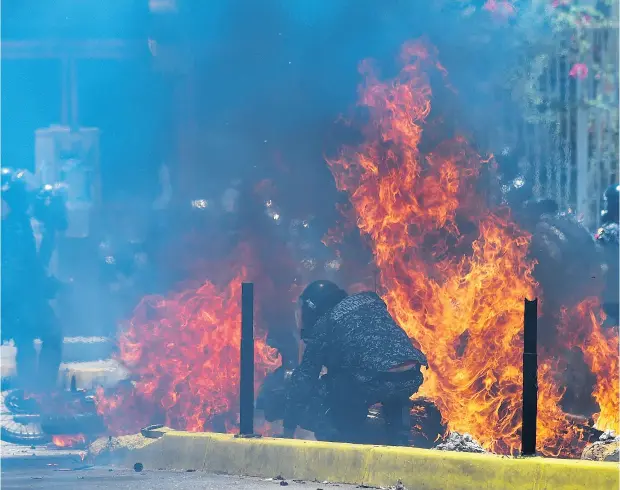  ?? JUAN BARRETO / AFP / GETTY IMAGES ?? Two police motorbikes burn after being hit by an improvised explosive device placed by anti-government activists during a protest in Caracas against the Venezuelan election on Sunday. Deadly violence erupted nationwide in the wake of the controvers­ial...