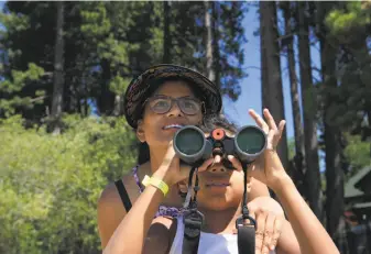  ??  ?? Amber More, 10, watches through binoculars as Angel nears the shore. Angel’s Tahoe crossing made her the youngest person to complete the California Triple Crown of Marathon Swimming.