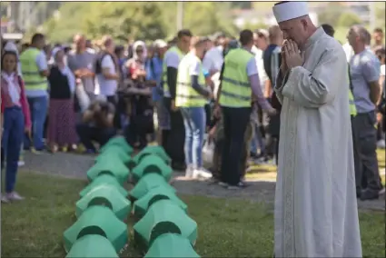  ?? AP PHOTO/DARKO BANDIC ?? A cleric prays above coffins at the memorial cemetery in Potocari near Srebrenica, Bosnia, on Thursday.