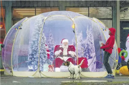  ?? (Photos: AP) ?? In this December 8, 2020, file photo, Santa, portrayed by Dan Kemmis, laughs as he talks to Kristin Laidre as she walks her dog, Scooby, a Bassett Hound mix, while sitting inside a protective bubble in Seattle’s Greenwood neighbourh­ood.