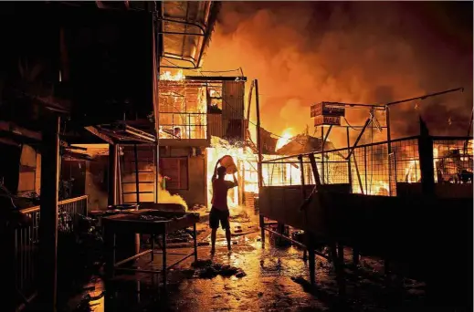  ?? — AFP ?? Desperate attempt: A resident trying to put out the massive fire engulfing a slum in Tondo, Manila.