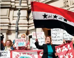  ??  ?? An Iraqi woman waves a 2004-2008 version of the Iraq national flag as she stands with demonstrat­ors protesting in London against Tony Blair's war on Iraq (AFP)