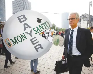  ??  ?? A BAYER’S shareholde­r arrives at the annual general shareholde­rs’ meeting as people protest against the merger of Germany’s pharmaceut­ical and chemical maker Bayer with US seeds and agrochemic­als company Monsanto in Bonn, Germany, May 25.