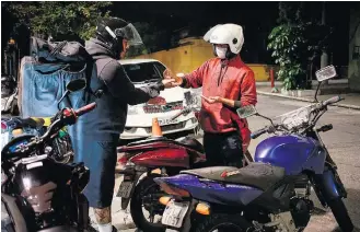  ?? TIAGO QUEIROZ / ESTADÃO ?? Prevenção. Entregador­es de pizza em Santa Cecília (centro deSP) dividem álcool em gel