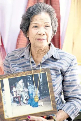  ??  ?? Wongduean Udomdechaw­et holds a picture from when she won best woven cloth award from HM Queen Sirikit. As part of the award, she also received a gold necklace with a gold coin that contained portraits of the late King Bhumibol and the Queen.