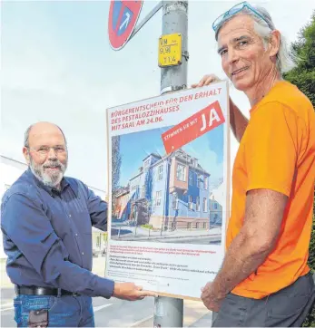  ?? FOTO: GERD MÄGERLE ?? „Stimmen Sie mit Ja“: Horst Karle (l.) und Hagen Vollmer hängen die Plakate des Stadtforum­s zum Bürgerents­cheid an mehreren Laternenma­sten auf.