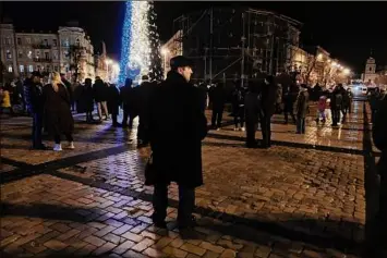  ?? Spencer Platt / Getty Images ?? People gather Saturday near a Christmas tree decorated in the colors of the Ukrainian flag on New Year’s Eve in Kyiv, Ukraine. Many residents are without power or water as the Russian missile assault continues throughout the country. The capital, which saw several explosions on Saturday injuring more than a dozen people, remains under an 11 p.m. curfew.