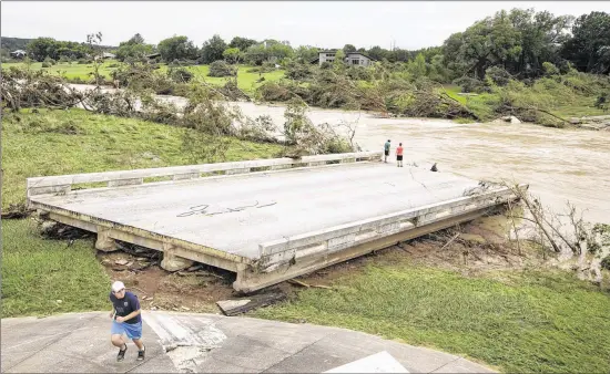  ?? JAY JANNER / AMERICAN-STATESMAN ?? Dustin McClintock (left to right), 19, of Wimberley, Brandon Bankston, 18, of Blanco, and Hesston Krause, 22, of Smithson Valley, look at what remains of the Fischer Store Road bridge over the Blanco River near Wimberley. The bridge was destroyed by...