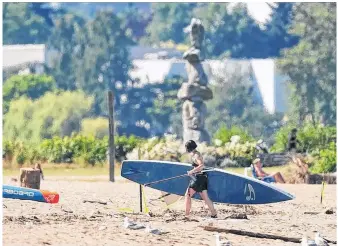  ?? POSTMEDIA NEWS ?? A surfer walks on the beach during record-breaking high temperatur­es at English Bay in Vancouver on Saturday.