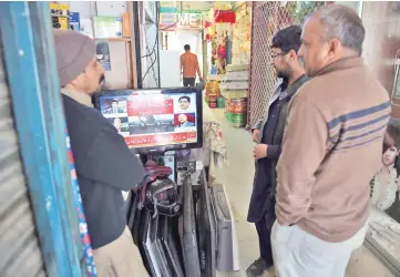  ??  ?? Pakistani shopkeeper­s watch a television broadcasti­ng breaking news in Islamabad.
