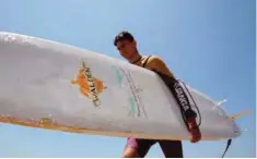  ??  ?? Ali Kassem carries his surfboard on a beach in the town of Jiyeh.—AFP photos