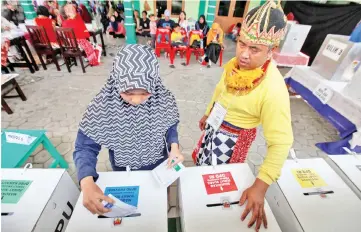  ?? — Reuters photo ?? An electoral official wearing a costume of a wayang character stands as a voter marks her ballots at a polling centre in Yogyakarta, Indonesia.