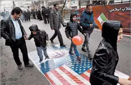  ?? VAHID SALEMI/AP ?? Iranians walk over a picture of President Donald Trump and the American flag during a rally in Tehran on Friday, marking the anniversar­y of the 1979 Islamic Revolution.