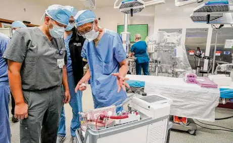  ?? Photos by Karen Warren/Staff photograph­er ?? Dr. Ju Kim, left, and Dr. Dewei Ren look at a donor heart beating inside a TransMedic­s device as the transplant team sets up.