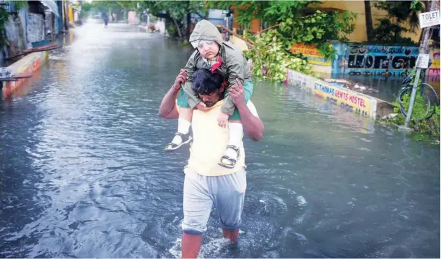  ?? Reuters ?? ↑
A man carries a child through a waterlogge­d road after Cyclone Nivar’s landfall in Chennai, Tamil Nadu, on Thursday.