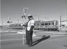  ??  ?? A flagger in Wheat Ridge stops traffic as a G-Line test train rolls by Jan. 2. The G-Line, which was supposed to start carrying passengers in the fall of 2016, has been delayed because it uses the same crossing technology as the A-Line.