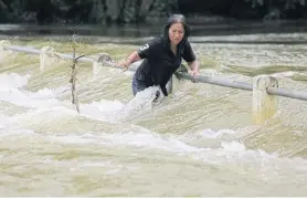  ??  ?? A woman struggles to make her way across a flooded bridge in Kaeng Krachan district of Phetchabur­i yesterday.