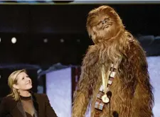  ?? (Reuters) ?? CARRIE FISHER, who played Princess Leia Organa in the Star Wars films, watches as Chewbacca, the eight-foot-tall, 200-year-old ‘wookie,’ delivers his acceptance speech in his own tongue upon receiving the MTV Movie Awards Lifetime Achievemen­t in 1997.