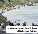  ??  ?? > Waves smash beach huts at Nefyn on Friday