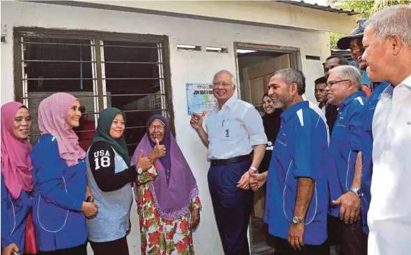  ?? BERNAMA PIC ?? Prime Minister Datuk Seri Najib Razak signing a plaque outside Saripah Kulup Samat’s (fourth from left) new house during the ‘Jom Bantu Rakyat’ programme in Kampung Pak Dollah, Kamunting, yesterday. With them is Bukit Gantang Umno chief Datuk Syed Abu Hussin Hafiz Syed Abdul Fasal (third from right).